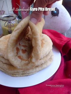 a person is holding up some food on a white plate with a red table cloth