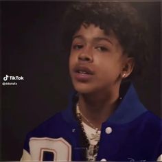 a young boy with curly hair wearing a jacket and beaded necklace, looking at the camera