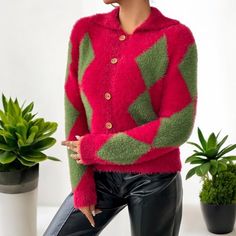 a woman wearing a red, green and pink argyle sweater standing in front of potted plants