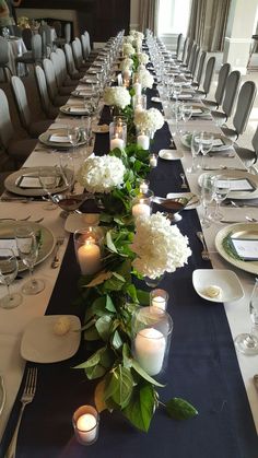 a long table is set with white flowers and candles for an elegant dinner or party