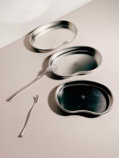 three metal pans and two spoons on a table