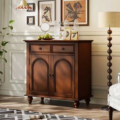 a wooden cabinet sitting next to a white chair in a room with pictures on the wall