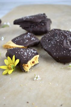 several pieces of chocolate and some yellow flowers on a piece of parchment paper with powdered sugar