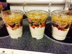 three glasses filled with yogurt and granola on top of a kitchen counter