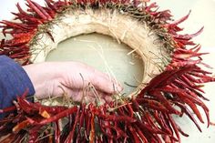 a person is holding a wreath made out of dried red chili peppers on a table