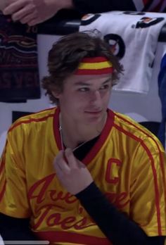 a young man wearing a yellow and red shirt sitting in front of a group of people