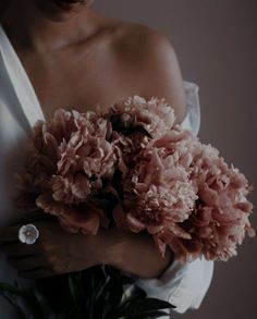 a woman in a white dress holding a bouquet of pink carnations and greenery