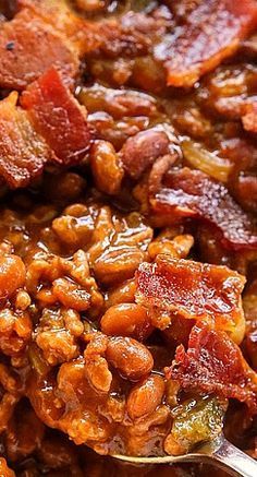 a spoon full of beans and bacon on top of a bowl with other food in it