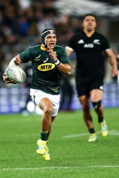 a rugby player runs with the ball in his hand as another man watches from the sidelines