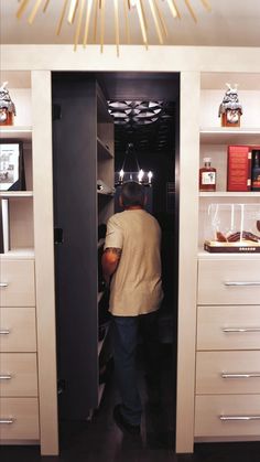 a man standing in front of a kitchen cabinet with drawers and lights on the ceiling