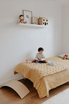 a young boy sitting on top of a bed next to a wooden shelf filled with toys