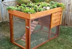 a wooden box with plants in it sitting on the grass next to a fenced area