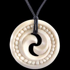 a white pendant with black spirals on a cord necklace hanging from a black background