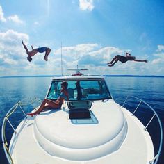 two people diving off the back of a boat in the ocean while another person dives into the water