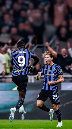 two soccer players running on the field with their hands in the air and people watching