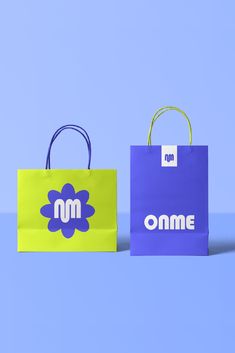 two shopping bags with the word omme printed on them are shown against a blue background