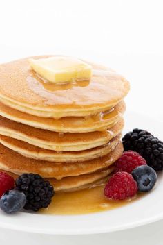 a stack of pancakes with syrup and berries on a white plate against a white background