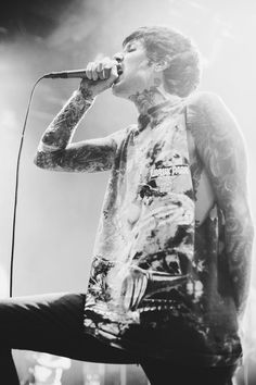 a man with tattoos on his arm and leg is singing into a microphone at a concert