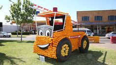 a truck made out of oranges sitting on top of a grass covered field in front of a building