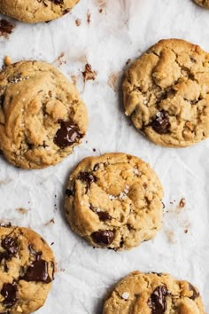 chocolate chip cookies are lined up on a piece of parchment paper, ready to be eaten