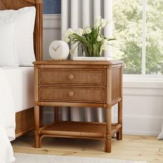 a nightstand with flowers on top of it next to a bed