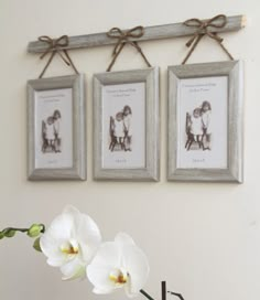 three framed pictures hang on the wall above a vase with flowers in it and two white orchids