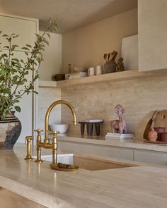 a kitchen counter with gold faucet and vases on the shelf above it