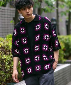 a young man wearing a black and purple crochet sweater is walking down the street