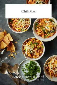 four bowls filled with different types of food on top of a gray table next to silverware