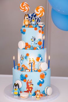 a three tiered blue cake with cartoon characters on it and candles in the shape of lollipops