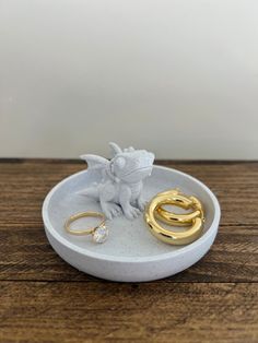 two gold rings sitting on top of a white plate next to a small dragon figurine