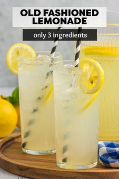 two glasses filled with lemonade sitting on top of a wooden tray next to lemons