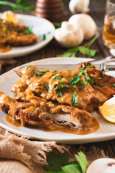 a white plate topped with meat covered in gravy next to lemon wedges