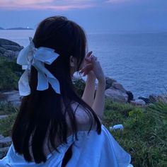 a woman sitting on top of a grass covered field next to the ocean