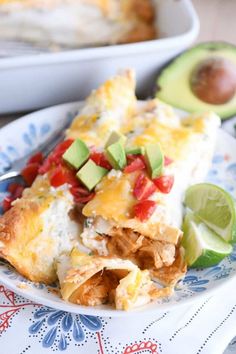 a slice of enchilada on a plate with avocado and tomatoes