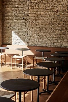 tables and stools are lined up against a brick wall with sunlight coming through the window