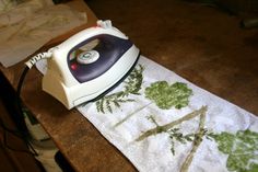 an iron sitting on top of a table next to a white and green towel with trees printed on it