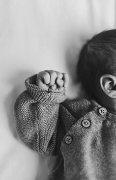 a black and white photo of a baby holding his hands up in the air while laying on a bed