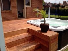 a hot tub sitting on top of a wooden deck next to a tree in a pot