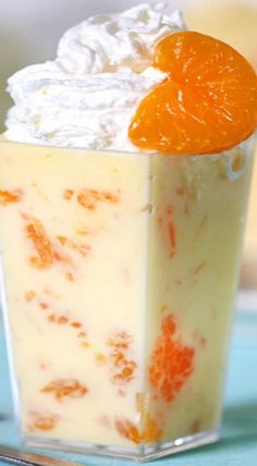 an orange dessert with whipped cream in a glass container on a blue tablecloth next to a fork