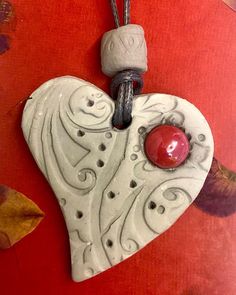 a white ceramic heart with a red bead hanging from it's side on a red background