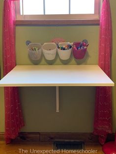 a white table with three bowls on it in front of a red chair and window