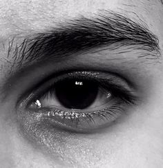 an extreme close up shot of the eye of a man with dark hair and black eyeshadow