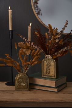 two candles are sitting on top of books and some dried plants in front of a mirror