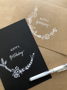 a birthday card and pen sitting on top of brown envelopes with white writing that says happy birthday