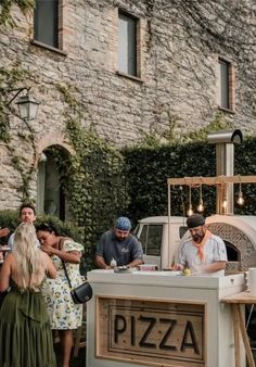 people are gathered around an outdoor pizza oven