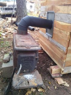 an old wood burning stove sitting in the woods next to a wooden building and trees