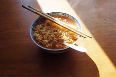 two chopsticks sticking out of a bowl of ramen with noodles on the table