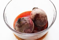 two plums sitting in a glass bowl on top of a white countertop next to a cork coaster