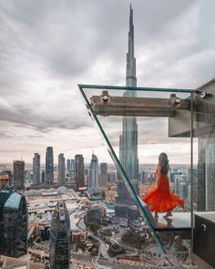 a woman in an orange dress standing on top of a building looking at the city